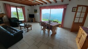 Un salon comprenant un canapé, une table à manger avec des chaises, un téléviseur et une vue sur l’extérieur.