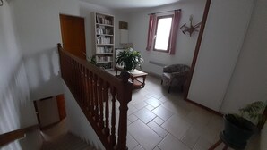 Un escalier avec une rampe en bois mène à un espace de vie comprenant une bibliothèque, un fauteuil et une plante en pot.