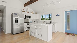 Une cuisine moderne avec des meubles blancs, des appareils en acier inoxydable et un îlot central doté de tabourets de bar.