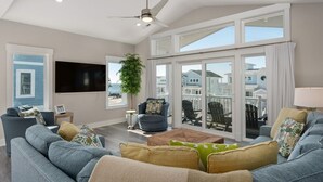 A spacious living room with a large window, a ceiling fan, and a flat-screen TV.