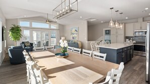 A modern kitchen with a central island, white cabinetry, stainless steel appliances, and a dining area with a wooden table and white chairs.