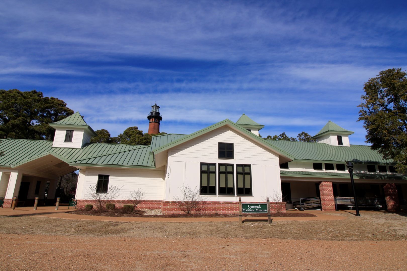 Un edificio blanco con techo verde y una estructura de faro, identificado como el Museo Marítimo de Currituck.