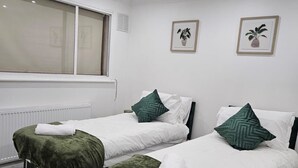 Une chambre d’hôtel avec deux lits, chacun recouvert d’une couverture verte assortie à des coussins, du linge de lit blanc et une fenêtre avec des stores.