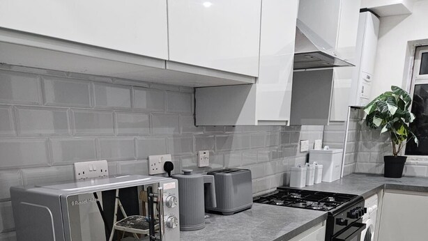 Une cuisine moderne avec des meubles gris, un plan de travail, une cuisinière, un grille-pain et un évier.
