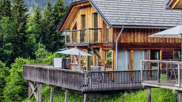 Eine Holzhütte mit Balkon und Sitzbereich im Freien, umgeben von Wald.