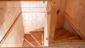 Una escalera de madera que baja a un nivel inferior, con barandilla de metal y una puerta con pomo.