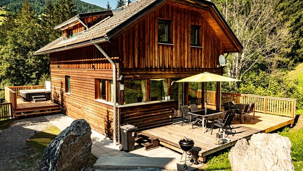 Una cabaña de madera con terraza, mobiliario exterior y una parrilla.