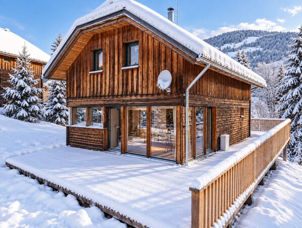 A wooden cabin with a large glass door entrance, a balcony, and a snow-covered roof. - Woody 8 - Chalet Bellevue with sauna and whirlpool (St. Georgen am Kreischberg)