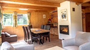 Un interior cálido de cabaña con techo de madera, comedor con mesa y sillas, sofá y chimenea.