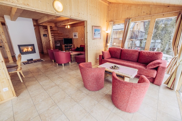 Un intérieur chaleureux en bois, avec une cheminée, des meubles rouges et une vue sur l’extérieur.