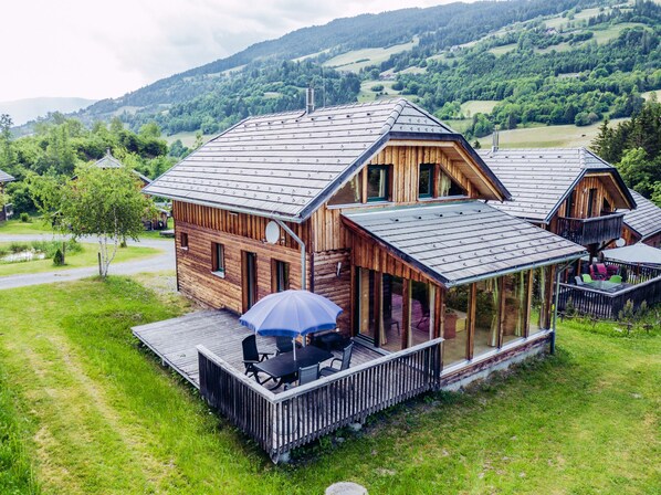 A wooden cabin with a deck and outdoor seating, surrounded by a lush green landscape.