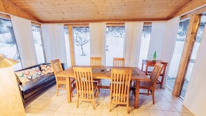 A wooden dining area with a table and chairs, large windows, and a view of a snowy landscape. - Woody 12 - with sauna & 2 cozy terraces (St. Georgen am Kreischberg)