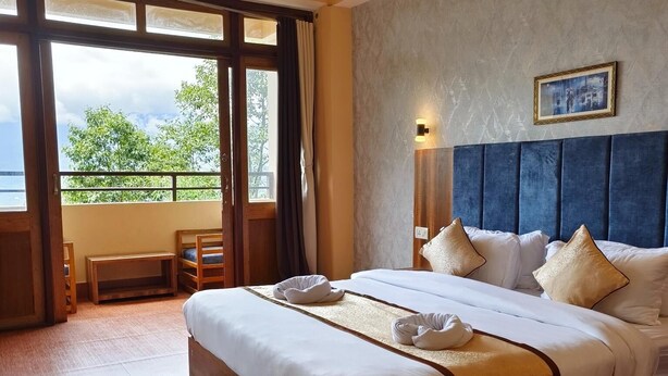 A hotel room with a large bed, a view of the outdoors, a wooden floor, and a green rug. - Aurora Gangtok (Gangtok)