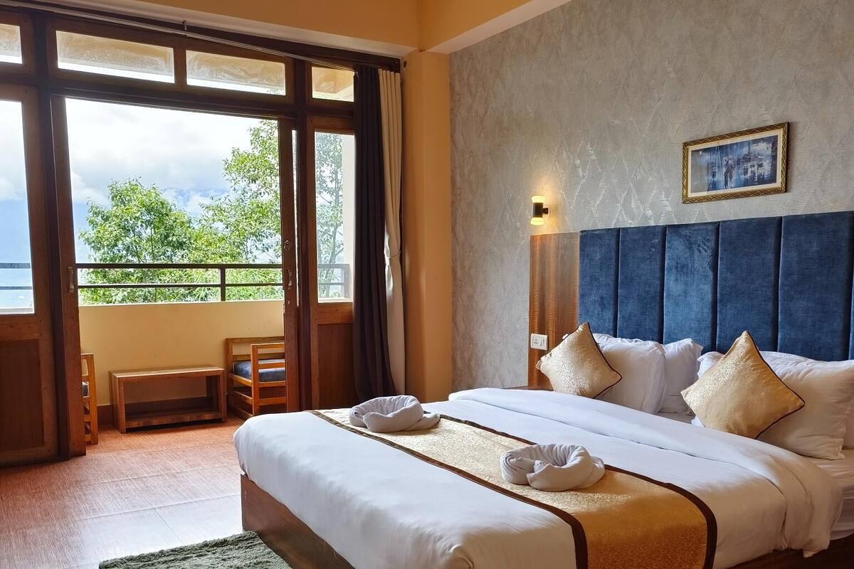 Hotellihuone, jossa on suuri sänky, näkymä ulos, puulattia ja vihreä matto.