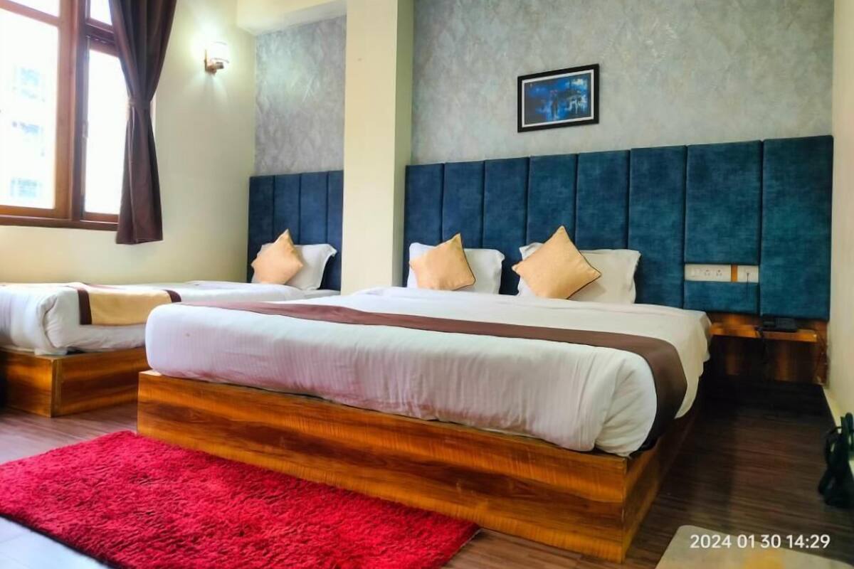 Hotellihuone, jossa on kaksi sänkyä, punainen matto, harmaa, kuvioitu seinä ja kehystetty taulu.