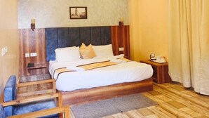 A bedroom with a large bed, wooden headboard, a small bedside table, a nightstand, a picture on the wall, and a staircase leading to an upper level. - Aurora Gangtok (Gangtok)