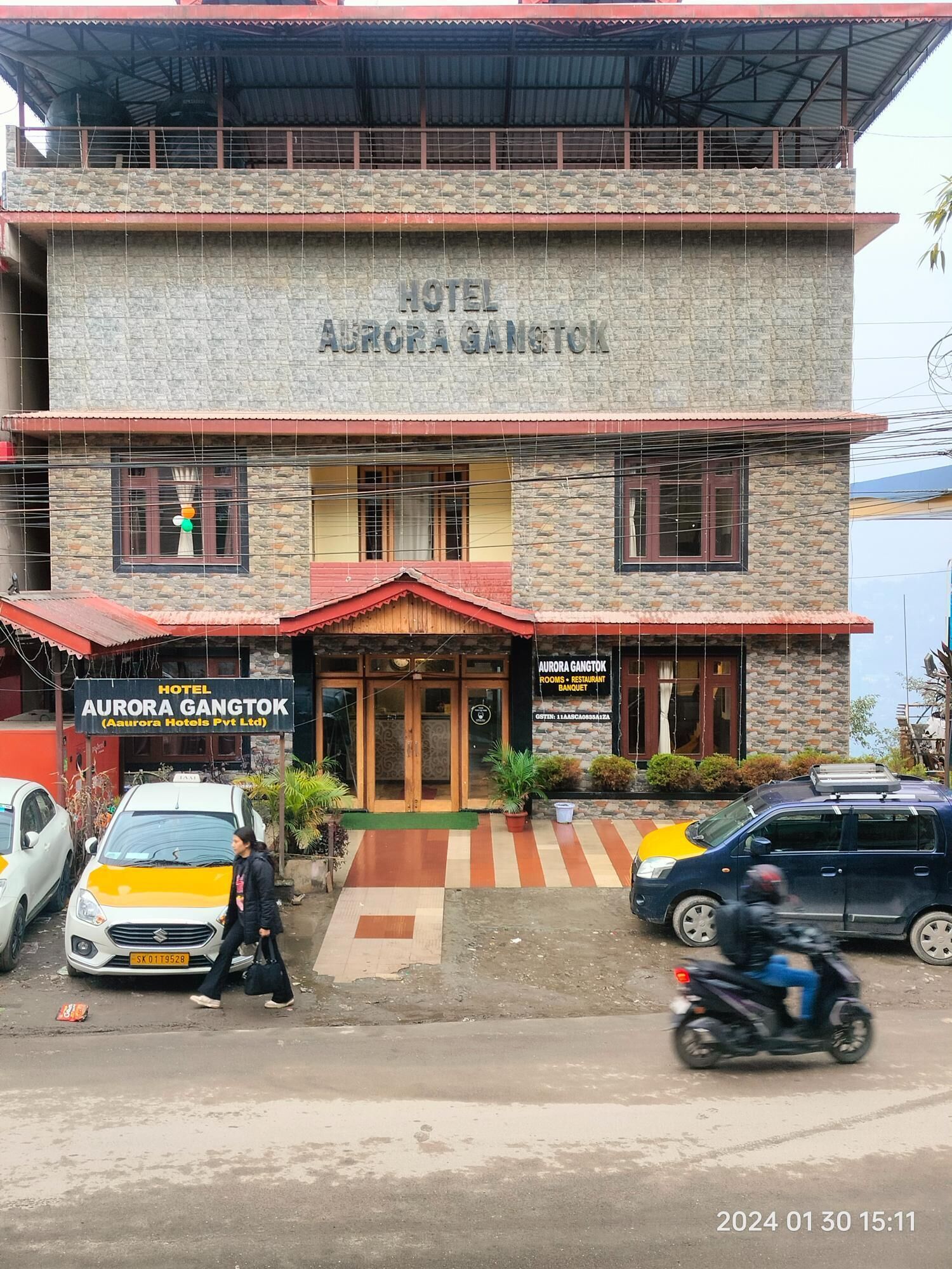 Un hotel de dos pisos llamado "Aurora Gangtok", con fachada de piedra y techo rojo.