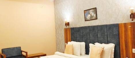 Quarto de hotel com uma cama grande, uma mesa de cabeceira de madeira, uma cadeira e uma obra de arte pendurada na parede.