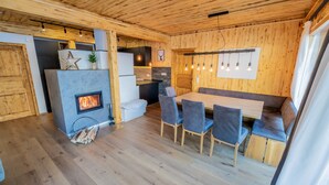 A cozy cabin interior with a fireplace, wooden walls, a dining area with chairs, and a kitchen with a refrigerator. - Woody 17 - Hillside Chalet Kreischberg (St. Georgen am Kreischberg)