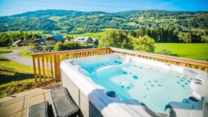 Un bain à remous sur une terrasse, avec vue sur un paysage verdoyant et des maisons.