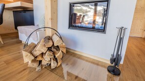 Une pièce avec un plancher en bois, une fenêtre donnant sur un paysage enneigé, une pile de bois de chauffage et un balai appuyé contre le mur.