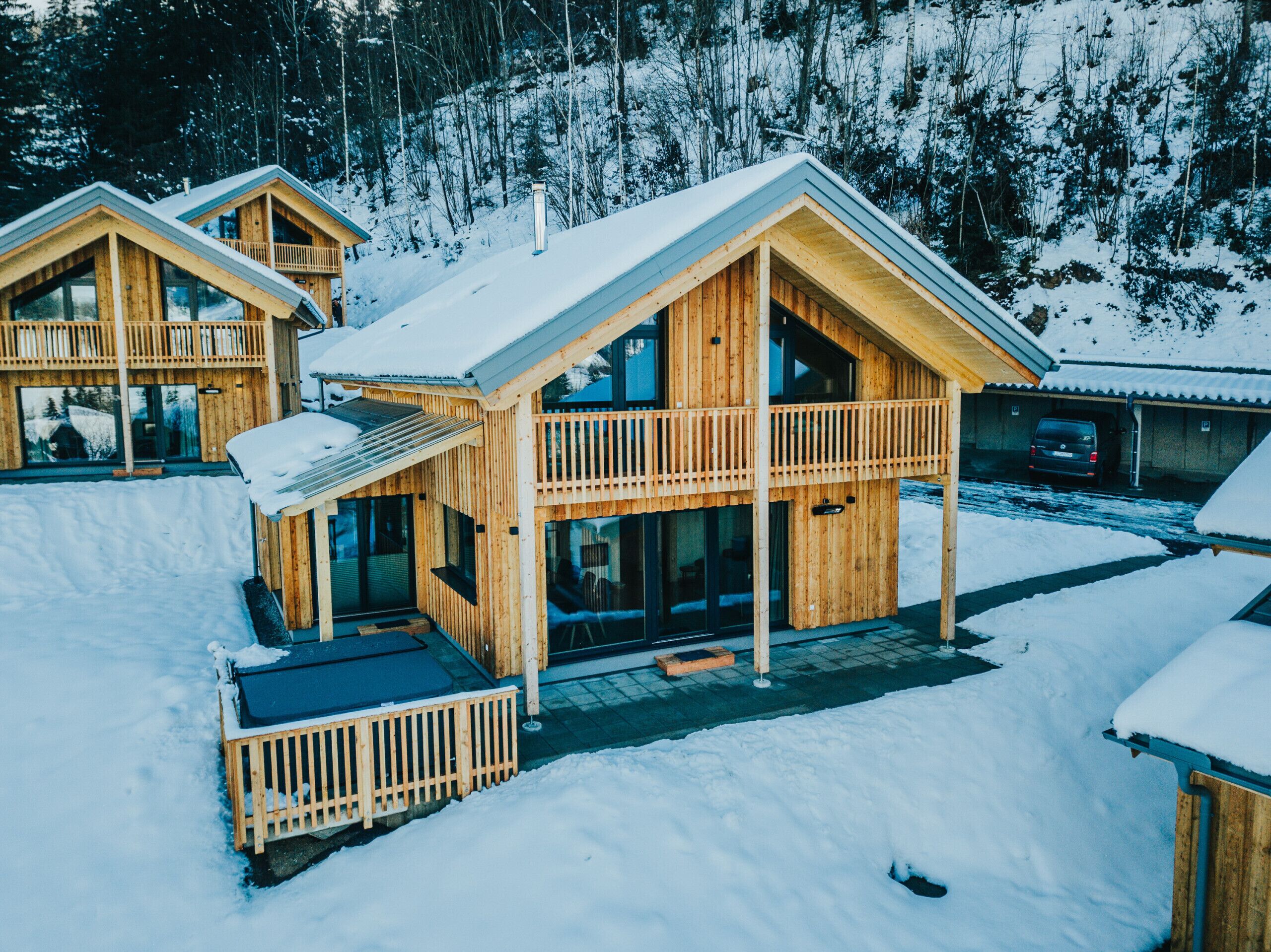 A wooden cabin with a balcony and a covered outdoor area, surrounded by snow.