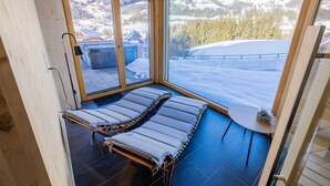 Une cabane en bois avec une porte en verre donnant sur un balcon équipé de deux chaises longues et d’une petite table agrémentée d’une plante.