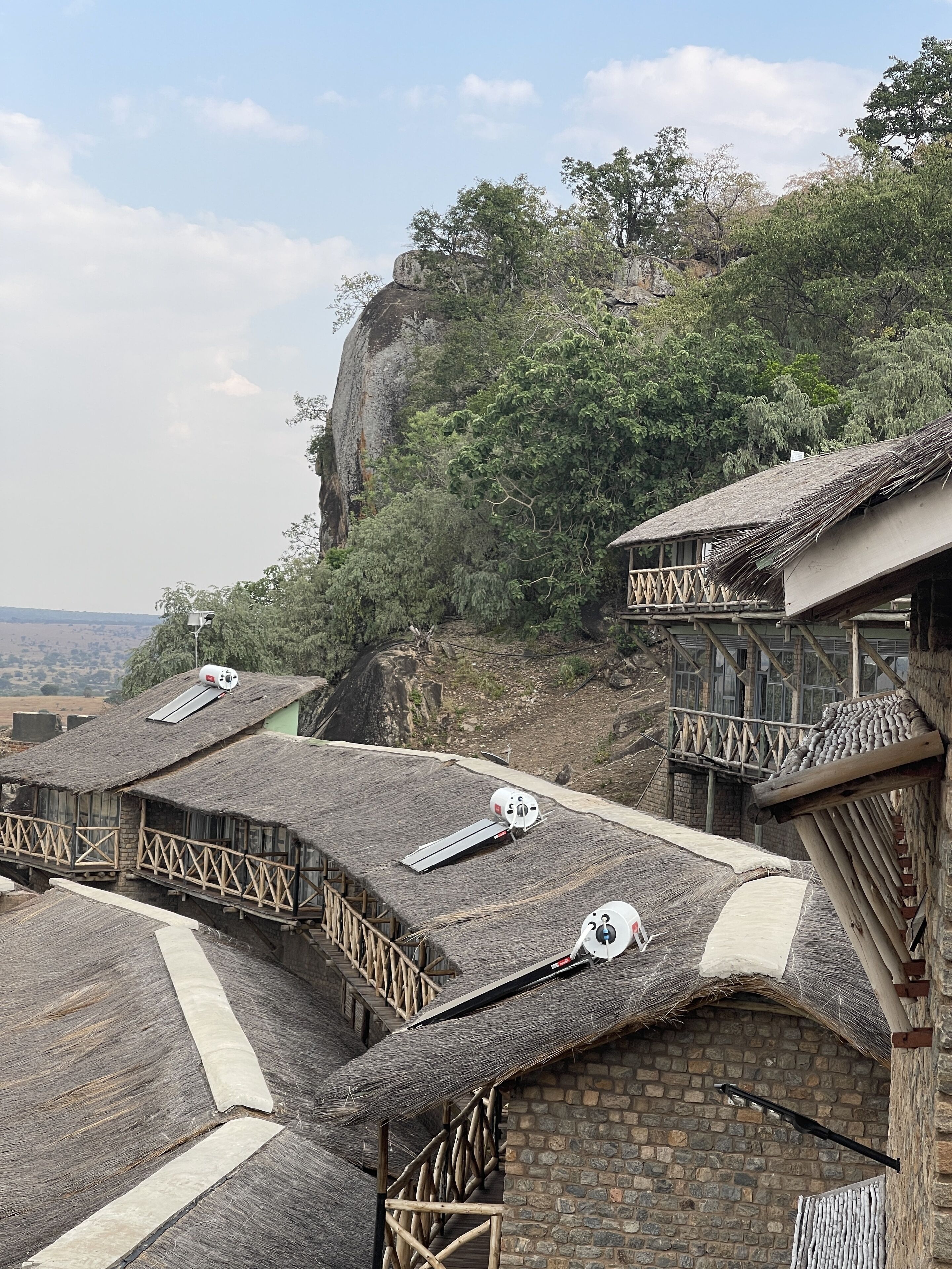 Edificio tradicional con techos de paja y barandillas de madera, ubicado en una ladera con vistas al paisaje.