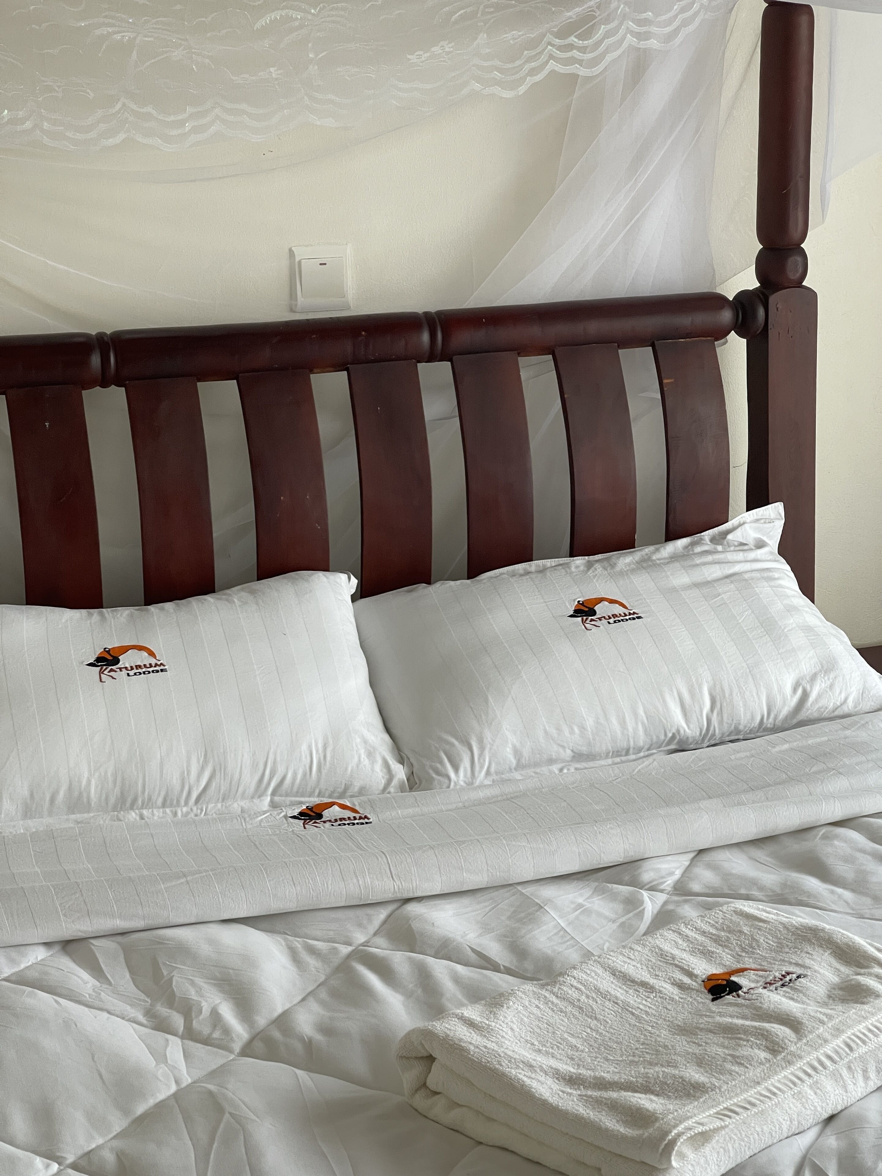 Una cama con cabecera de madera, dos almohadas con un logotipo y una colcha blanca.