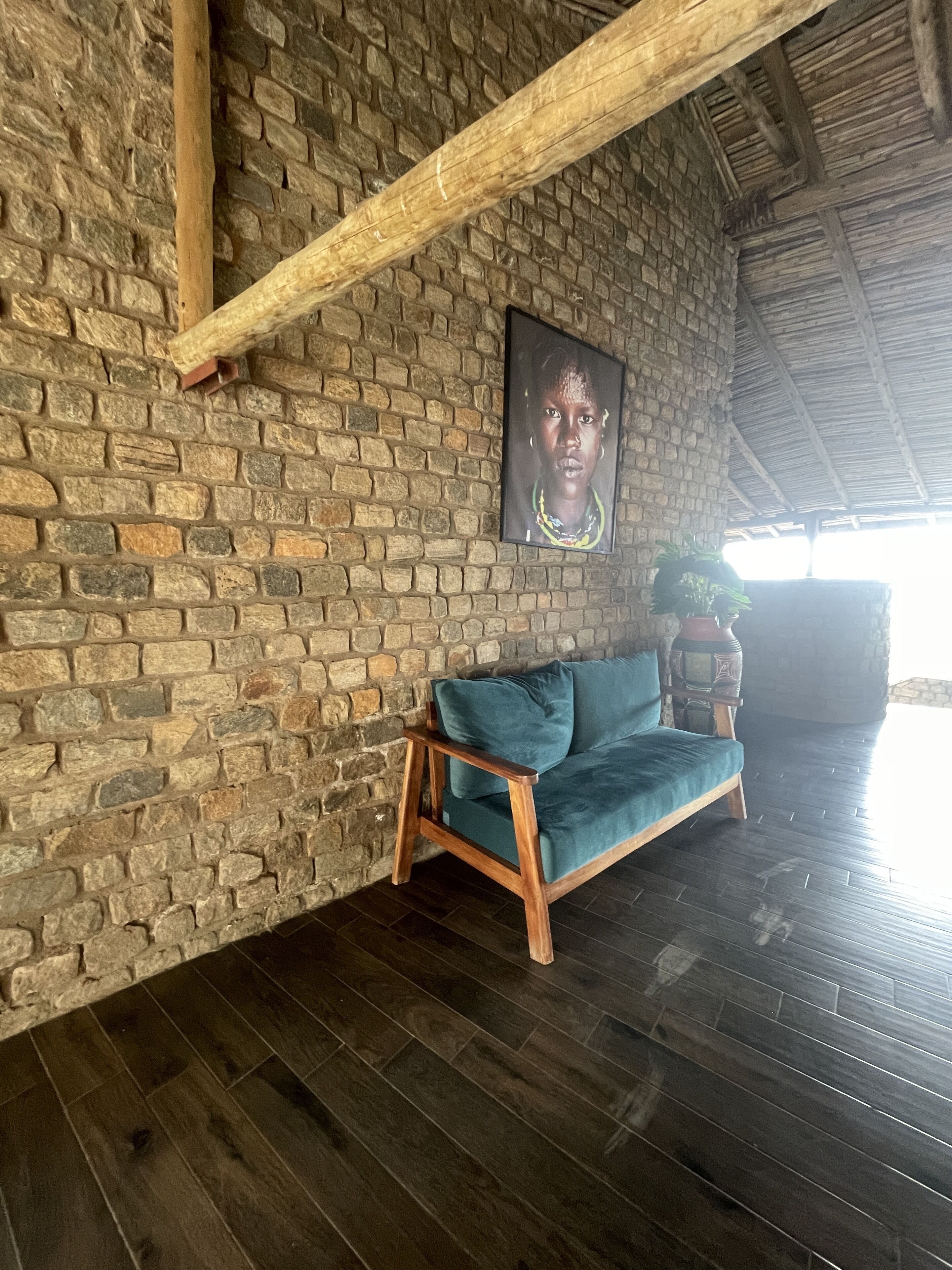 Una habitación con pared de piedra, techo de madera, sofá azul y un cuadro enmarcado en la pared.