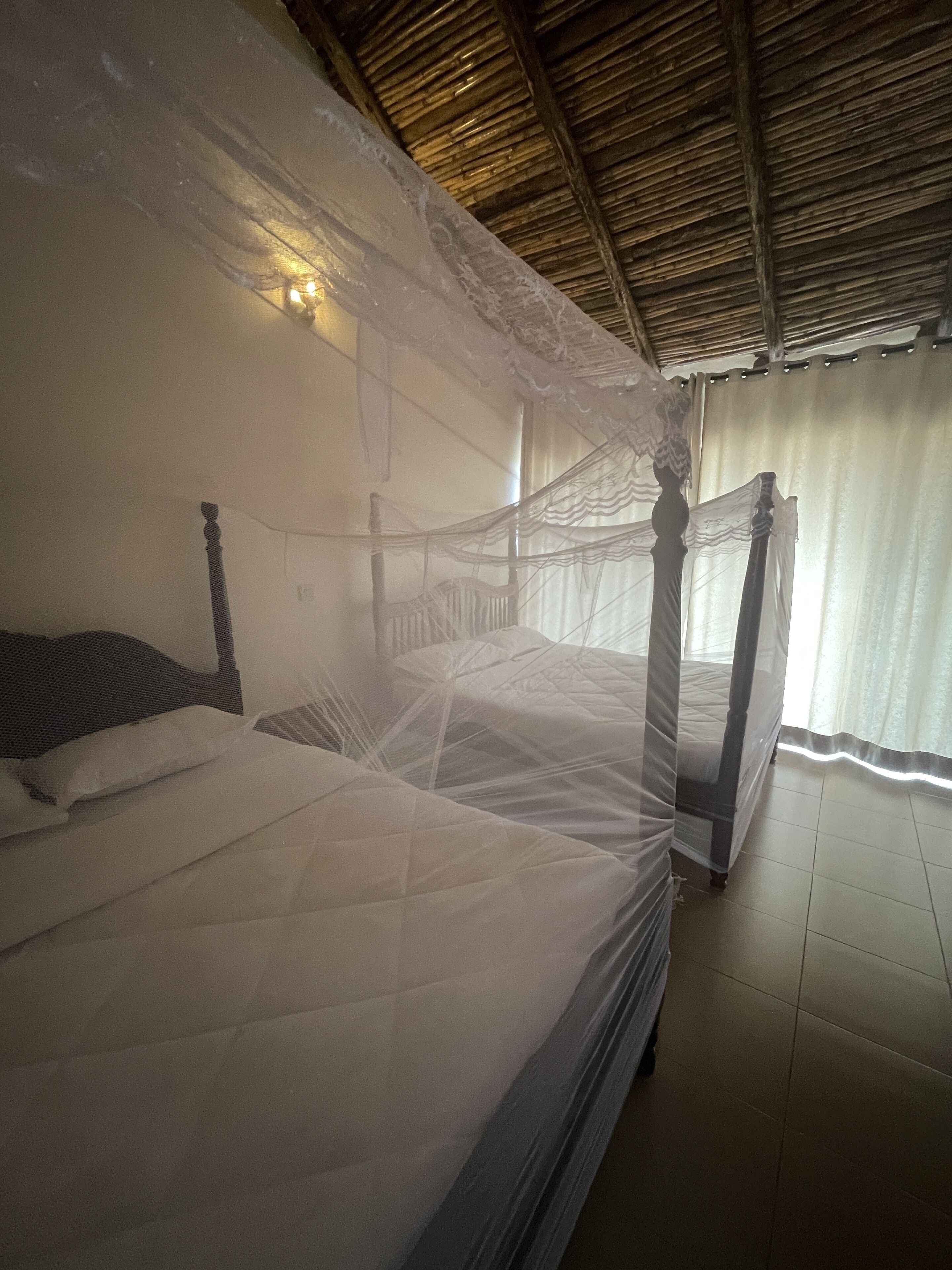 Una cama con dosel, mosquitera, cabecera de madera y una lámpara de pared.