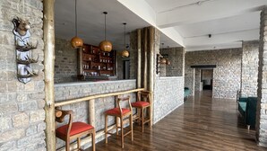 A spacious room with a wooden floor, stone walls, and a bar area with stools. - Katurum Lodge Kidepo  (Loitanit)