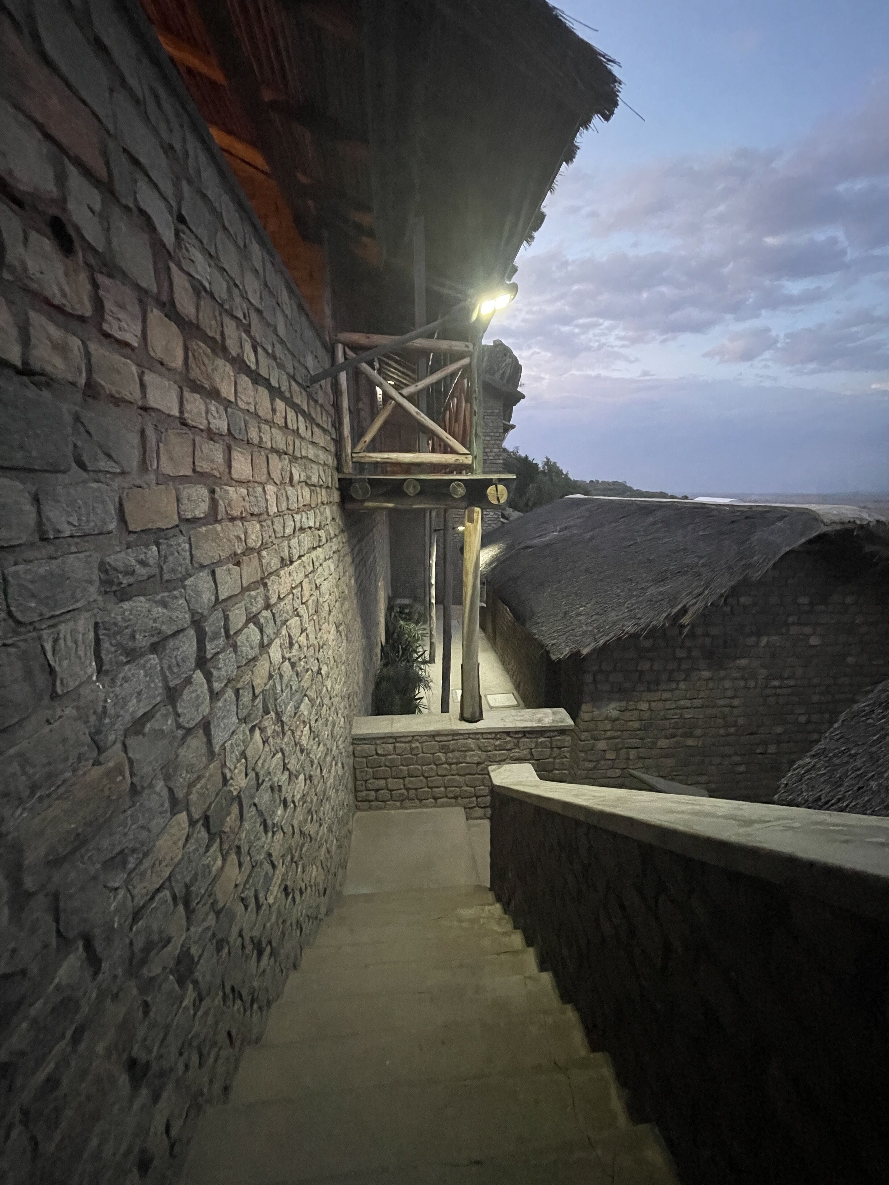 Una estrecha escalera de piedra que conduce a una construcción de madera con techo de paja, rodeada de muros de piedra.