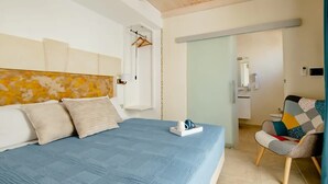 A bedroom with a bed, a chair, a hanging coat rack, and a bathroom visible through an open door. - Sirocco Suite with private terrace (Tuglie)