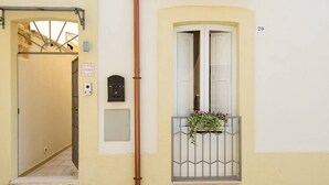 A narrow hallway leading to a door, a window with a metal grille, and a wall-mounted light switch. - Sirocco Suite with private terrace (Tuglie)