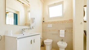 A bathroom with a white vanity, a toilet, and a bidet. There is a window above the toilet and a mirror above the vanity. - Sirocco Suite with private terrace (Tuglie)