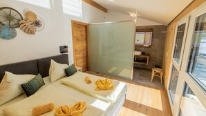 A modern hotel room with a bed, a glass shower enclosure, a small bathroom, and a view through a large window.