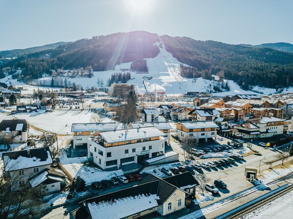 Une ville avec une station de ski en arrière-plan, où l’on trouve un mélange de bâtiments modernes et traditionnels, un parking et une voie ferrée.