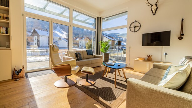 A spacious living room with a large window, a sofa, a chair, a coffee table, and a television.