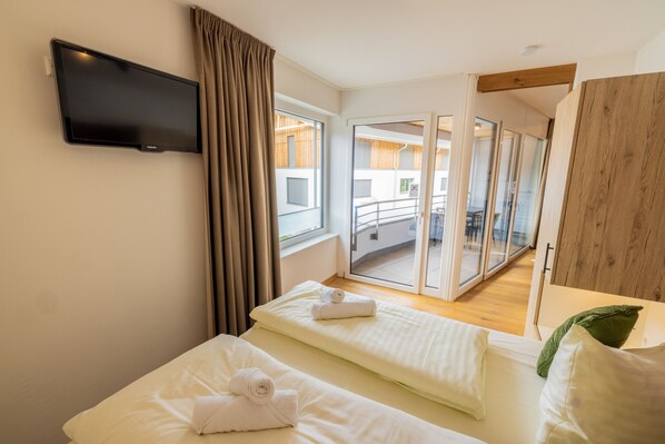 Ett hotellrum med två sängar, en tv som är monterad på väggen och utsikt över balkongen.