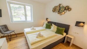 Une chambre à coucher avec un grand lit, deux tables de chevet, une chaise et une fenêtre donnant sur un paysage verdoyant.