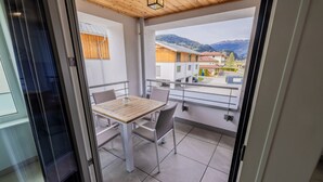 A balcony with a table and chairs, a view of buildings and mountains, and a wooden ceiling.