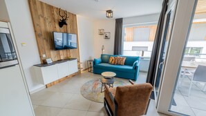 A modern living room with a blue sofa, a brown armchair, a flat-screen TV, and a wooden accent wall with a mounted deer head.