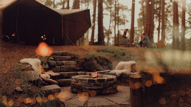 A stone fire pit with seating, surrounded by a forested area and a tent. - The Dell of Abernethy (Nethy Bridge)