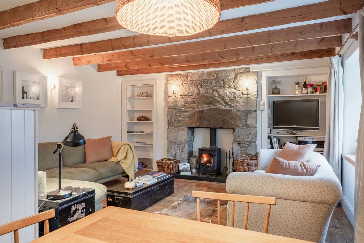 A cozy living room with a stone fireplace, wooden beams, a sofa, a table, and a television.
