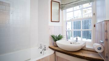 A bathroom with a bathtub, a sink, a mirror, and a window.