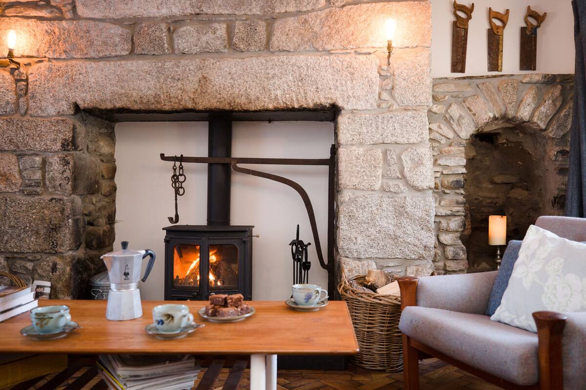 A cozy room with a stone fireplace, a wooden table with tea cups and a coffee pot, and a comfortable armchair.