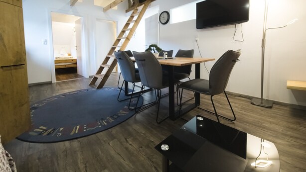 Un espace repas moderne avec une table en bois, des chaises noires, une table basse noire et un plancher en bois.