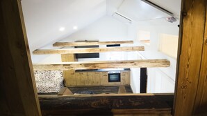 Une chambre de style « loft », avec des poutres apparentes en bois, un coin cuisine et une grande fenêtre.