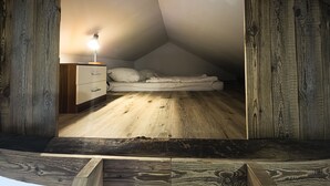 Une petite chambre à coucher de style mansardé, avec un plafond en bois, un lit simple, une table de chevet et une lampe de bureau.